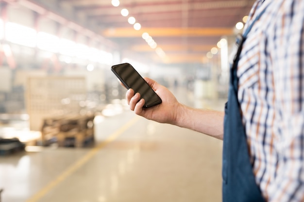 Modernes Gerät mit Touchscreen, gehalten von einem jungen Ingenieur oder Techniker in der Arbeitskleidung, die SMS am Arbeitsplatz sendet