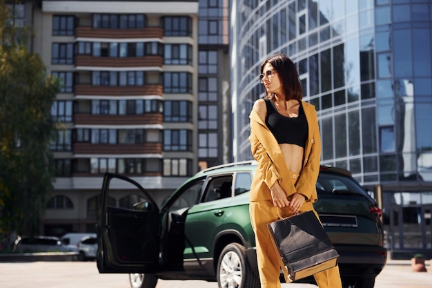 Modernes Geschäftsgebäude im Hintergrund Junge modische Frau in weinrotem Mantel tagsüber mit ihrem Auto