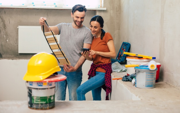 Modernes glückliches junges Paar verliebt in Freizeitkleidung während der Reparatur oder Renovierung von Wänden mit vielen Werkzeugen dafür