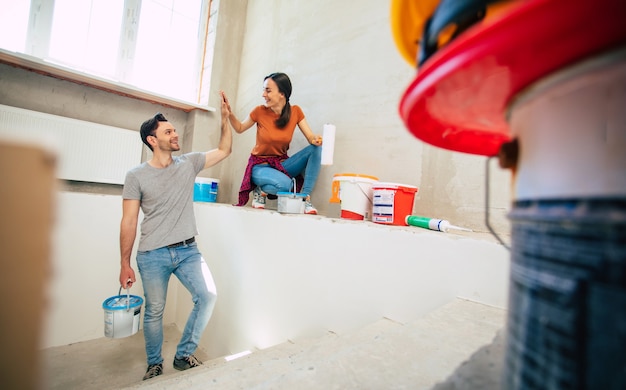 Modernes glückliches junges Paar verliebt in Freizeitkleidung während der Reparatur oder Renovierung von Wänden mit vielen Werkzeugen dafür