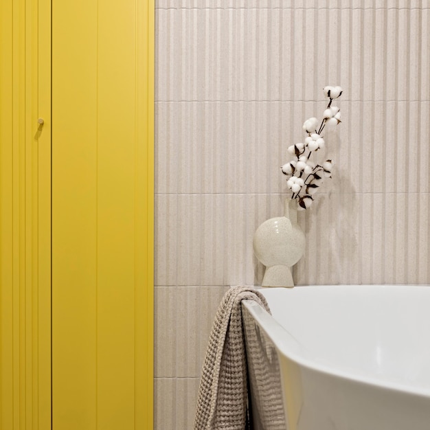 Modernes helles und gelbes Badezimmer mit Lamellenwand Großes weißes Bad mit braunem Handtuch und getrockneten Blumen
