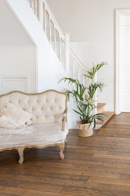Modernes Interieur eines hellen Zimmers in einer zweistöckigen Wohnung mit Dekorationsgegenständen im Bali-Stil mit Balkon. weiße Wände, Holzböden und Vintage-Möbel