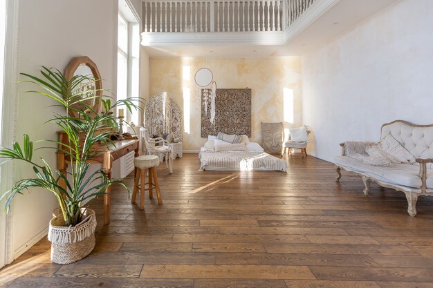 Modernes Interieur eines hellen Zimmers in einer zweistöckigen Wohnung mit Dekorationsgegenständen im Bali-Stil mit Balkon. weiße Wände, Holzböden und Vintage-Möbel