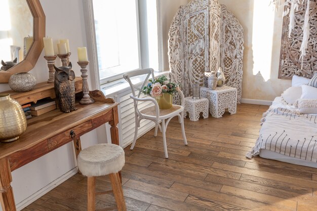 Modernes Interieur eines hellen Zimmers in einer zweistöckigen Wohnung mit Dekorationsgegenständen im Bali-Stil mit Balkon. weiße Wände, Holzböden und Vintage-Möbel