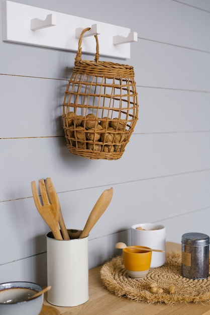 Modernes Kücheninterieur mit grauer Holzvertäfelung im skandinavischen Stil an der Wand, Walnüssen im Korb, Geschirr und Küchenutensilien