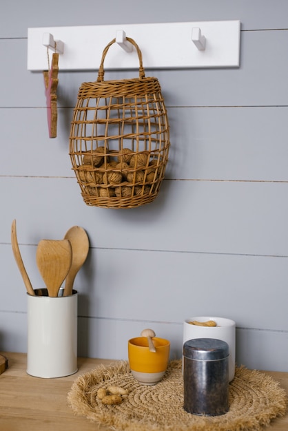 Modernes Kücheninterieur mit grauer Holzvertäfelung im skandinavischen Stil an der Wand, Walnüssen im Korb, Geschirr und Küchenutensilien