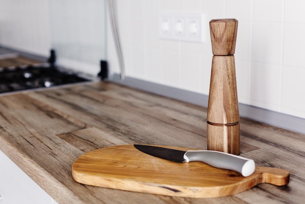 Modernes Messer auf Holzschneidebrett mit Pfeffergewürz auf Holztischplatte Kochen auf moderner Küche mit Möbeln in grauer Farbe Graue Schränke im skandinavischen Stil Hausmannskost