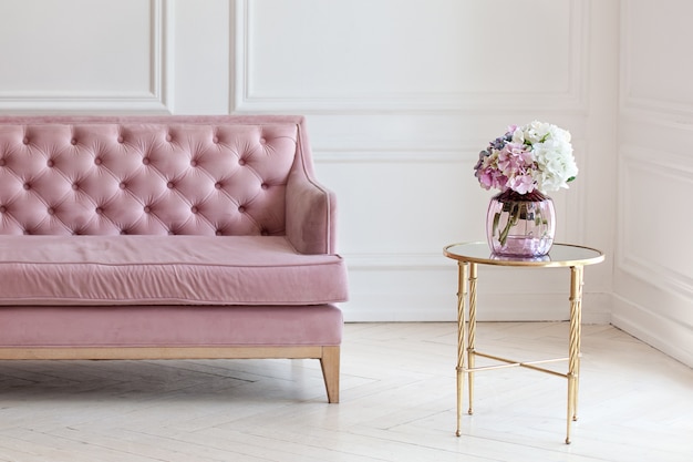 Modernes minimalistisches Wohnzimmer Interieur mit rosa Sofa und Couchtisch mit Vase Blumenstrauß Hortensia gegen weiße Wand.