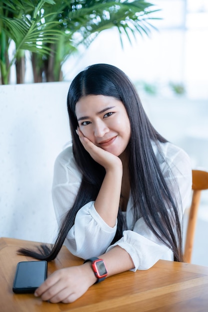 Modernes porträt der schönen glücklichen asiatischen reisenden, die smartwatch trägt, die schönes weißes kleid trägt und jeans-lebensstil trägt, der im sitzenden café-restauranthintergrund genießt