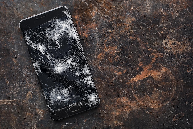 Modernes Smartphone mit großem kaputtem Bildschirm mit Trümmern auf dem Grunge-Hintergrund mit Kopierraum