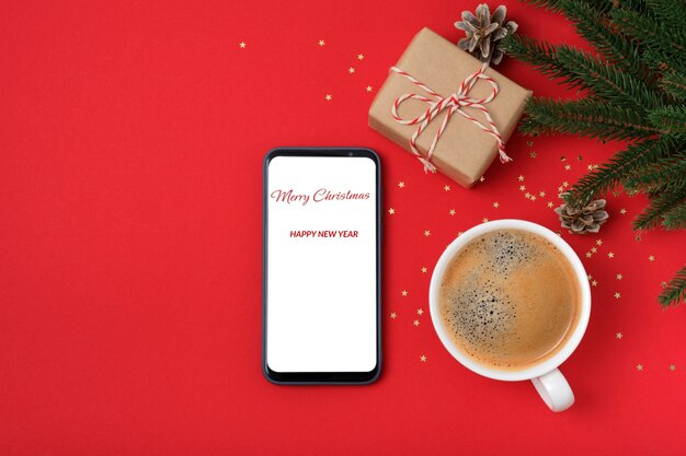 Modernes Smartphone mit Modell auf rotem Hintergrund mit Weihnachtsdekoration. Flache Lay-Vorlage. Goldene Sterne, Geschenkbox