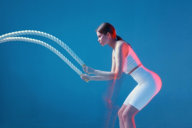Modernes Sportmädchen-Training mit wehenden weißen Seilen auf blauem Hintergrund mit Bewegungsunschärfe im Kopierraum