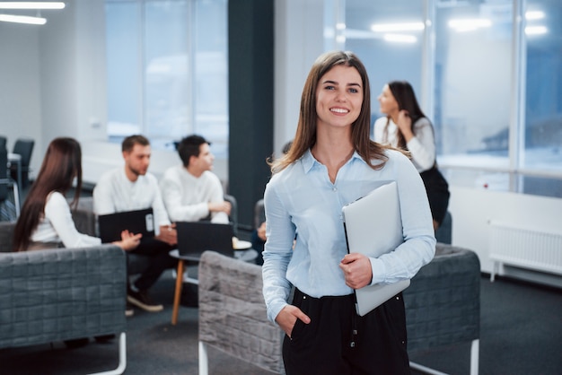 Modernes Startup-Unternehmen. Porträt des jungen Mädchens steht im Büro mit Angestellten im Hintergrund