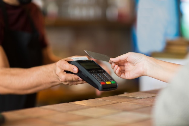 modernes Technologie- und Menschenkonzept - Mann oder Barkeeper mit Zahlungsterminal und Kundenhand mit Kreditkarte an der Bar des Cafés