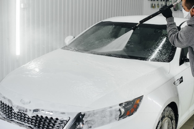 Modernes Waschen mit Schaum und Hochdruckwasser eines weißen Autos. Autowäsche.