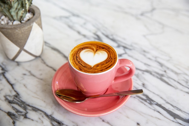 Moderno copo-de-rosa de cappuccino quente no fundo da mesa de mármore. Arte com leite em forma de coração para o símbolo do amor. Uma xícara para a rotina matinal.