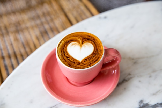 Moderno copo-de-rosa de cappuccino quente no fundo da mesa de mármore. Arte com leite em forma de coração para o símbolo do amor. Uma xícara para a rotina matinal.