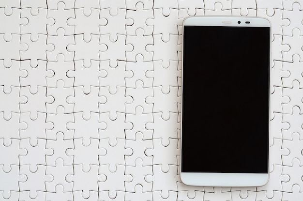 Un moderno y gran teléfono inteligente con pantalla táctil se encuentra en un rompecabezas blanco.