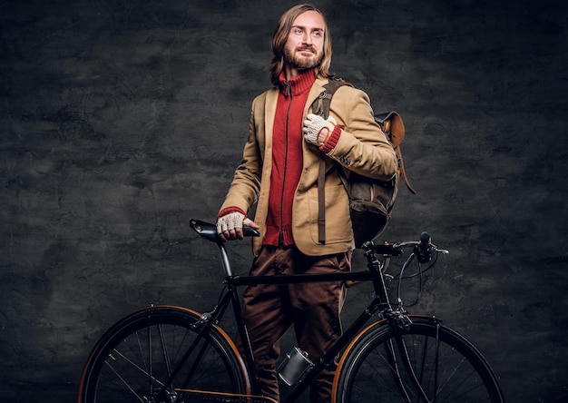 Moderno hipster barbudo de suéter vermelho está segurando sua bicicleta enquanto posava para o fotógrafo.