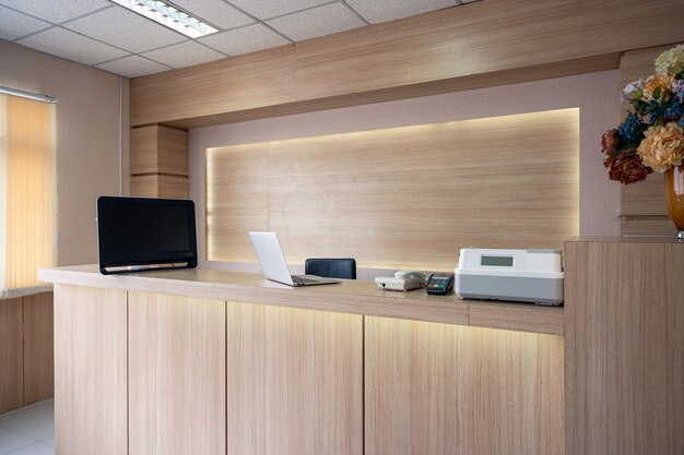 Moderno mostrador de recepción de madera con monitor portátil y dispositivo electrónico en el hospital