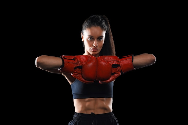 Foto moderno con mujer de kickboxing en ropa deportiva y guantes de kickboxing mirándote listo para luchar sobre fondo negro para un diseño de estilo de vida saludable. deporte, estilo de vida saludable.