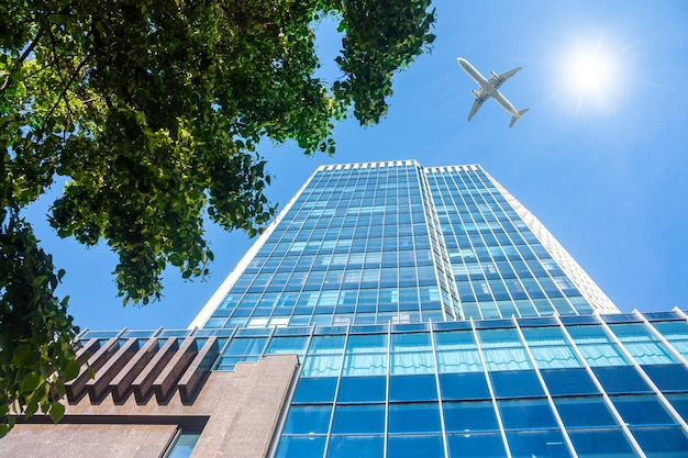 Un moderno rascacielos de oficinas y un avión de pasajeros blanco sobrevolando este edificio