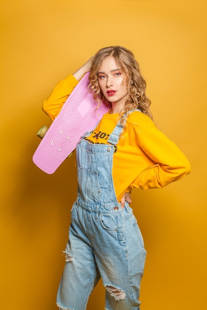 Modewoman hält ein rosa Skateboard auf einem leuchtend gelben Hintergrund