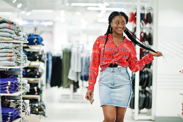 Modische afrikanisch-amerikanische Frau in rotem Hemd und Jeansrock posierte im Bekleidungsgeschäft Es ist Zeit zum Einkaufen