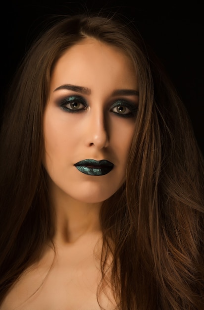 Modische Brunettefrau mit perfekter Haut und kreativem metallisch-grünem Make-up. Nahaufnahmeportrait im Studio auf dunklem Hintergrund