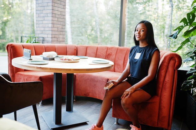 Modische feministische Afroamerikanerin in schwarzem T-Shirt und Shorts, posiert im Restaurant.