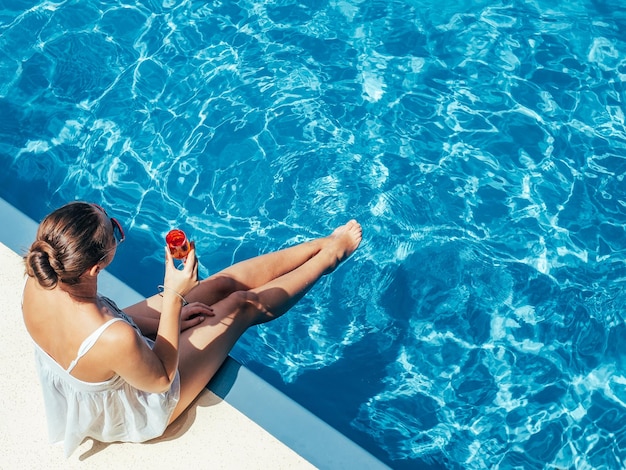 Modische Frau, die am Pool auf dem leeren Deck sitzt