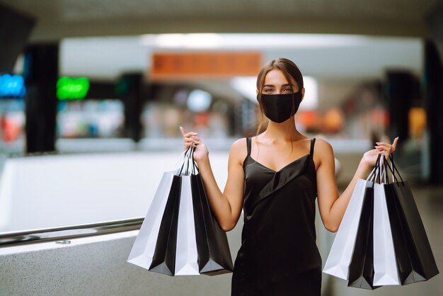 Modische Frau, die medizinische Schutzmaske mit Einkaufstaschen im Einkaufszentrum trägt.