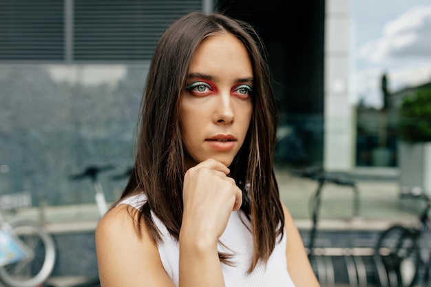 Modische Frau mit hellem Mode-Make-up posiert draußen vor der Kamera vor Stadthintergrund