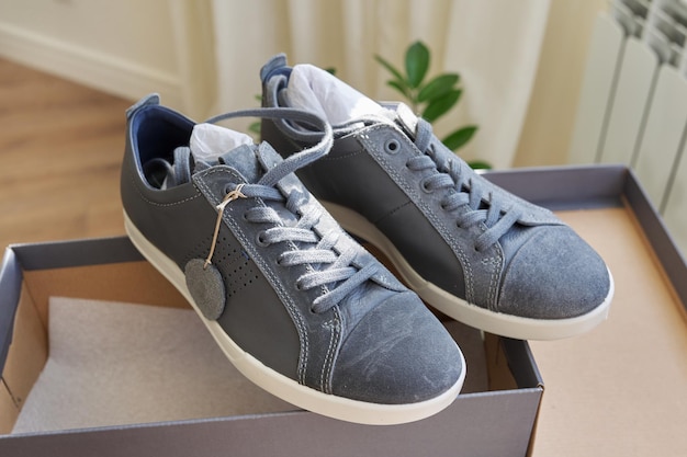Modische Herren-Sneaker aus grauem Leder, lässiges Design. Neues Paar Schuhe aus der Kiste ausgepackt, Online-Shopping, Saisonschlussverkauf, Herrenschuh-Trends, Kiste mit Turnschuhen zu Hause