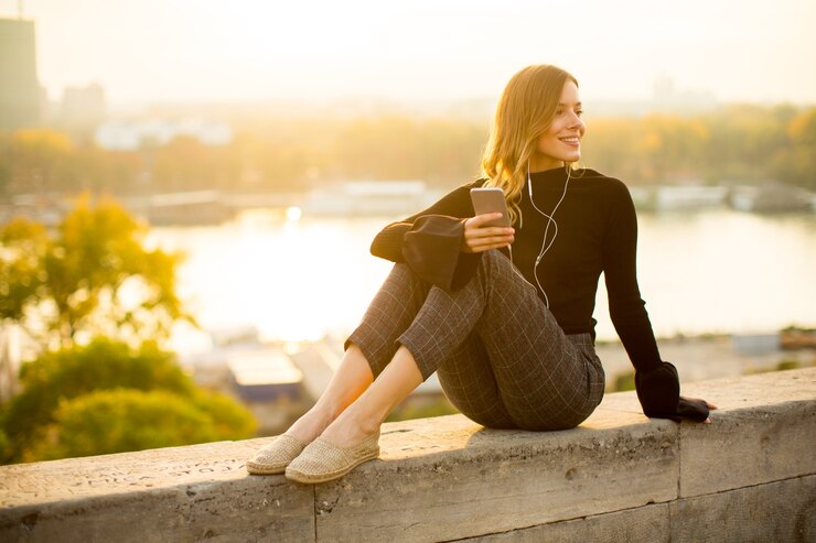 Foto modische hörende musik der jungen frau vom smartphone im freien bei sonnenuntergang