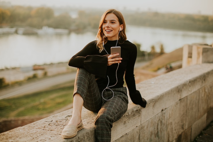 Foto modische hörende musik der jungen frau vom smartphone im freien bei sonnenuntergang