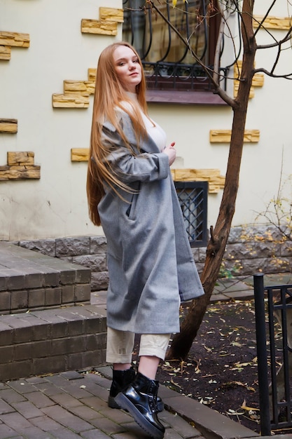 Modische junge schöne stilvolle Frau im grauen Mantel zu Fuß auf der Straße. Herbstmodetrend für lächelnde, glückliche, zielstrebige Frauen. Konzeptstil, Mode, Schönheit und Leistungsziele. Platz kopieren