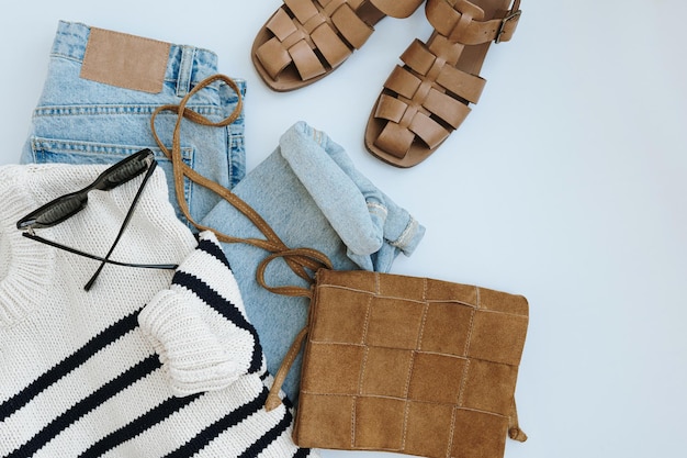 Modische Mode-Collage mit weiblicher Kleidung und Accessoires Ledersandalen Suede Schultertasche blaue Jeans gestreifter Pullover auf weißem Hintergrund mit Copyspace Flat Lay Top View