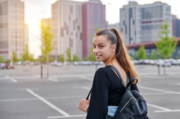 Modische schöne lächelnde Teenagerin in kurzen Hosen mit Rucksack in die Kamera blickend