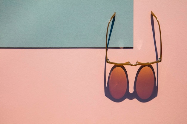 Modische Sommersonnenbrille mit langem Schatten auf rosa und blauem Hintergrund