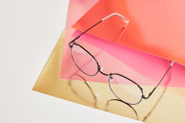 Modische trendige Augenbrillen zur Korrektur der Sehkraft auf kreativem Hintergrund, bunter rosa und goldener glänzender Kartonhintergrund, Kopierraum