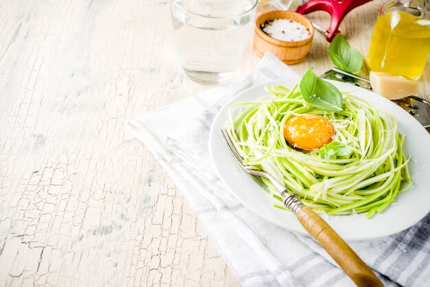 Modische vegane Lebensmittelrezepte, Käse-Zucchini-Spaghettiteigwaren mit Eigelb mit Parmesankäse, Olivenöl und Basilikumblättern, Leichtbetonoberfläche