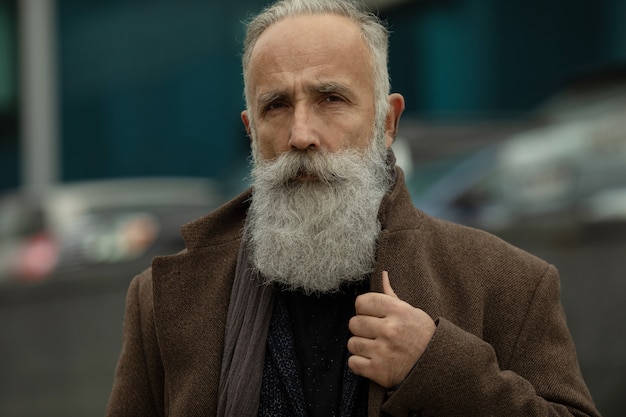 Modischer älterer Mann mit grauem Haar und Bart ist draußen auf der Straße.