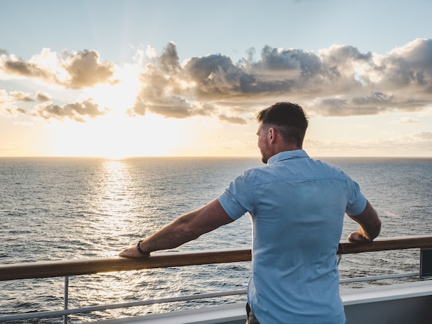 Modischer Mann auf dem leeren Deck eines Kreuzfahrtschiffes vor dem Hintergrund der Meereswellen.