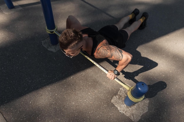 Foto modischer, stylischer, gut aussehender, muskulöser typ mit sonnenbrille und kopfhörern in schwarzer sportbekleidung, der auf der straße auftaucht athletischer mann mit tattoo-training und training