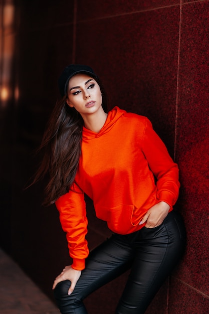 Modisches brünettes Mädchen in einem leuchtend orangefarbenen Pullover.