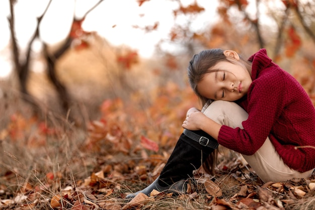 Modisches Kind 5 Jahre alt posiert im Herbstpark. kleines Mädchen sitzt in gefallenen Blättern