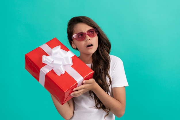 Modisches, neugieriges Kind mit Sonnenbrille hält die Neugier der Geschenkbox aufrecht
