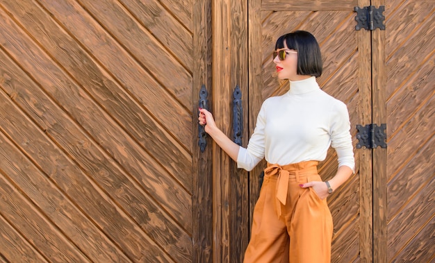 Modisches Outfit schlanke große Dame. Mode- und Stilkonzept. Frauenspaziergang im eleganten Outfit. Moderner Brunette der Frau stehen im Freien hölzerner Hintergrund. Mädchen mit Make-up posiert in modischer Kleidung.