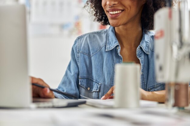 Modista afroamericana profesional trabaja en un portátil moderno sentado en el lugar de trabajo